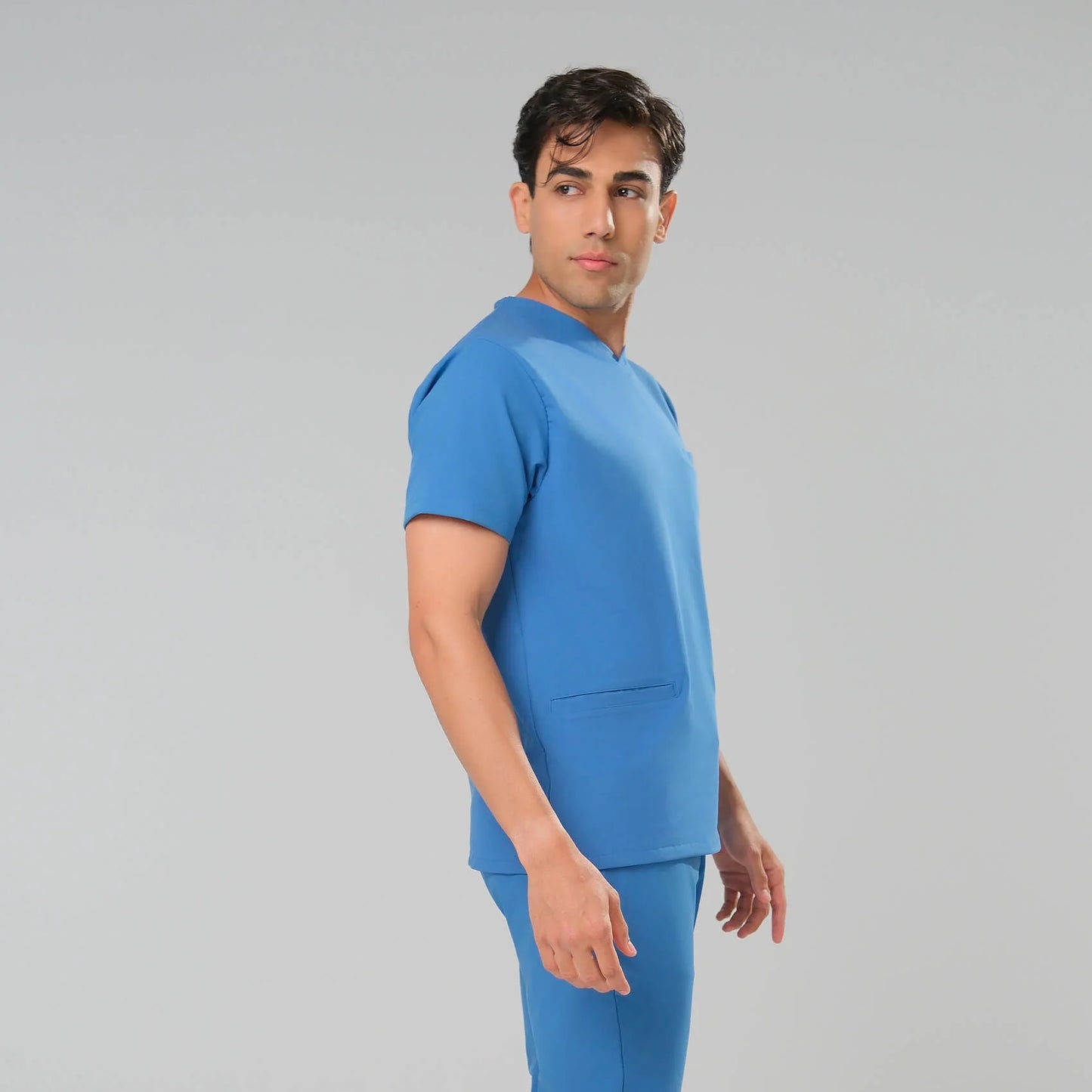 Man wearing light blue scrub set against a grey background
