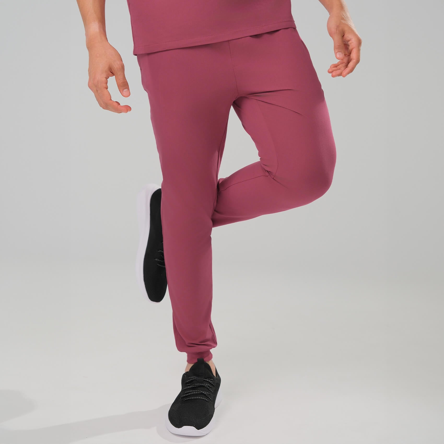 man wearing red scrub joggers with black shoes on a light grey background