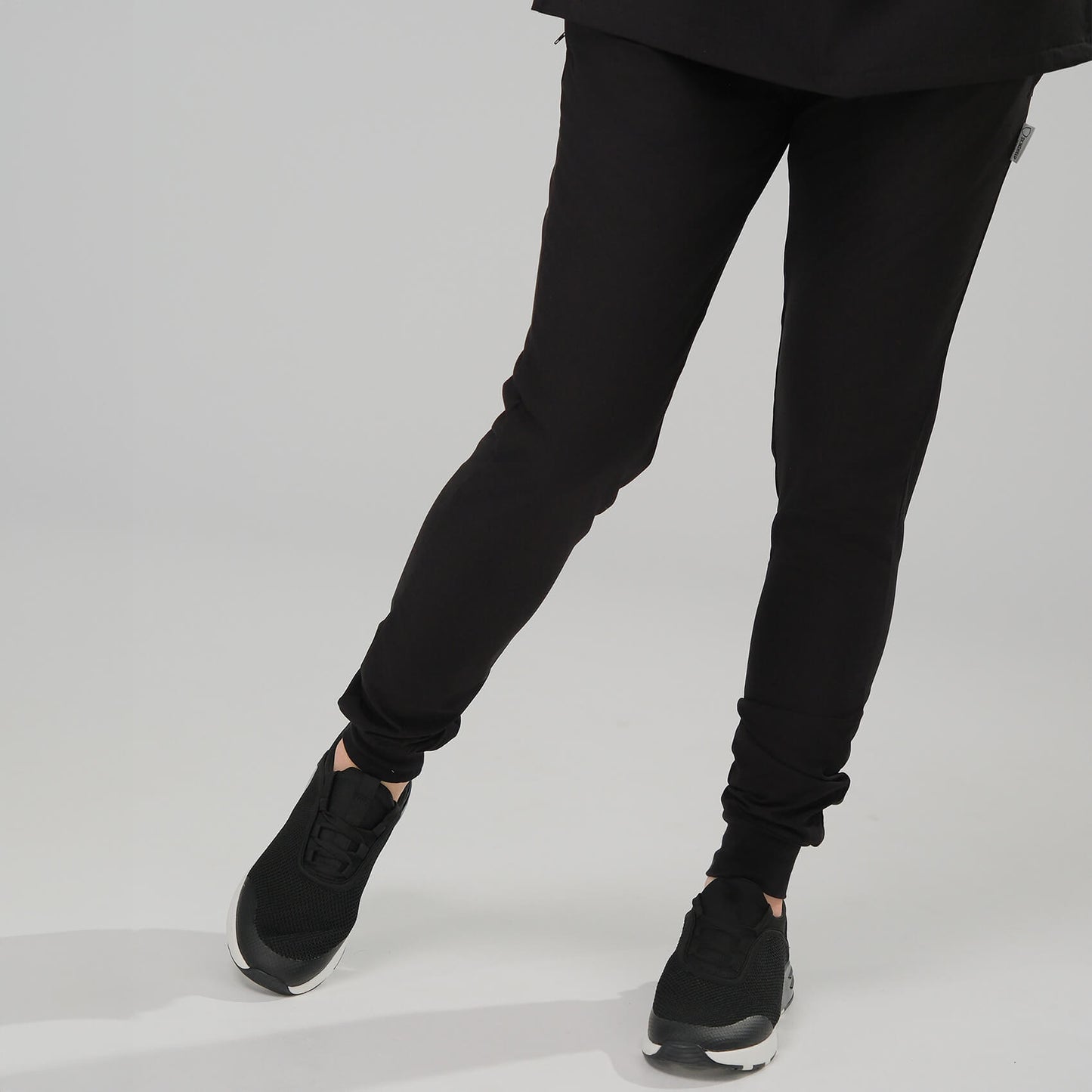 Lady wearing black jogger scrubs and black trainers on a light grey background