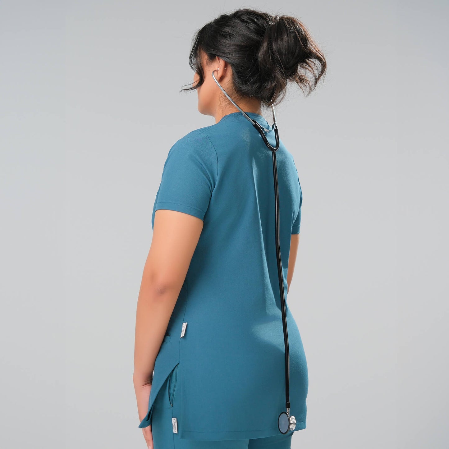 Lady wearing green medical scrubs with a stethoscope on a grey background