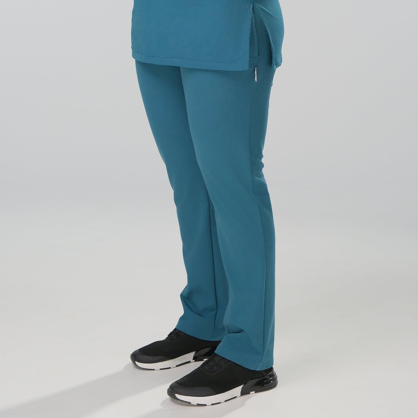 Woman wearing teal scrubs with black shoes on a white background