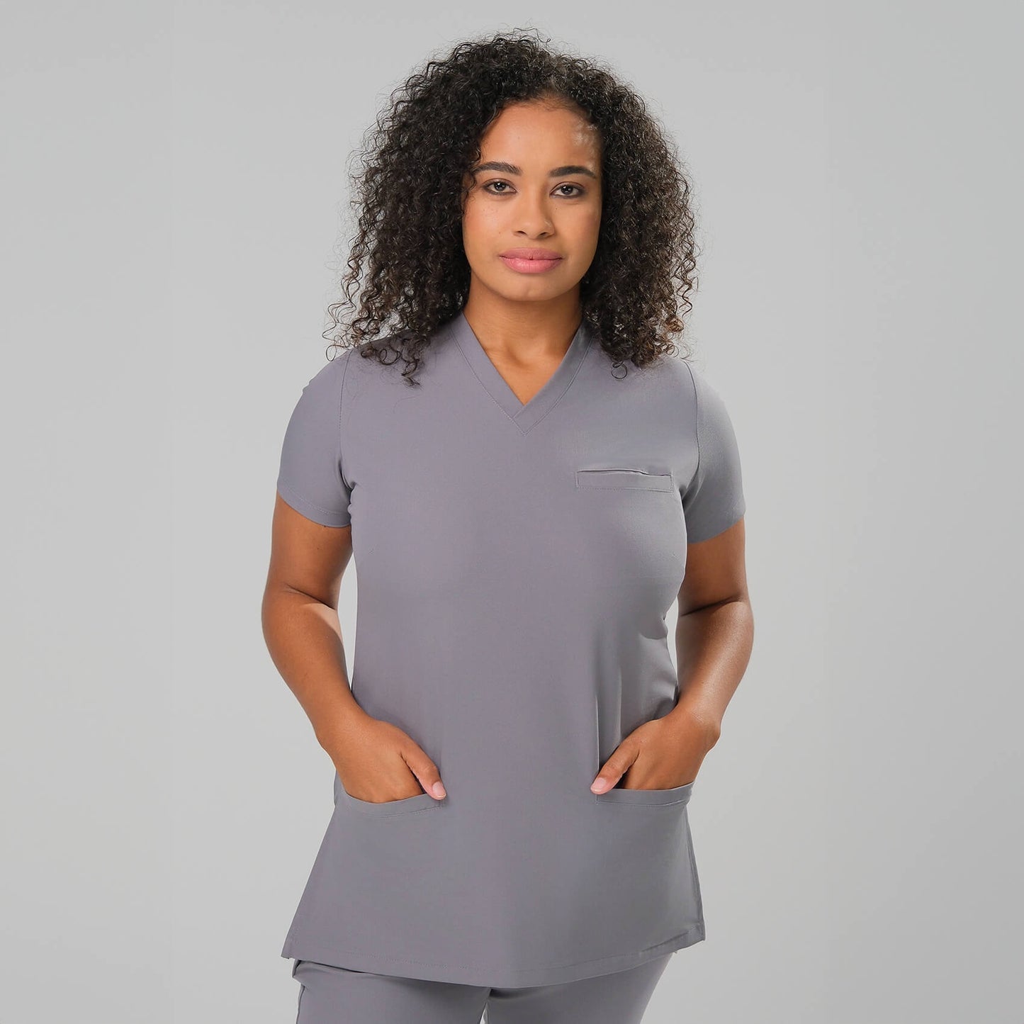 Woman wearing a grey scrub top and pants on a plain background
