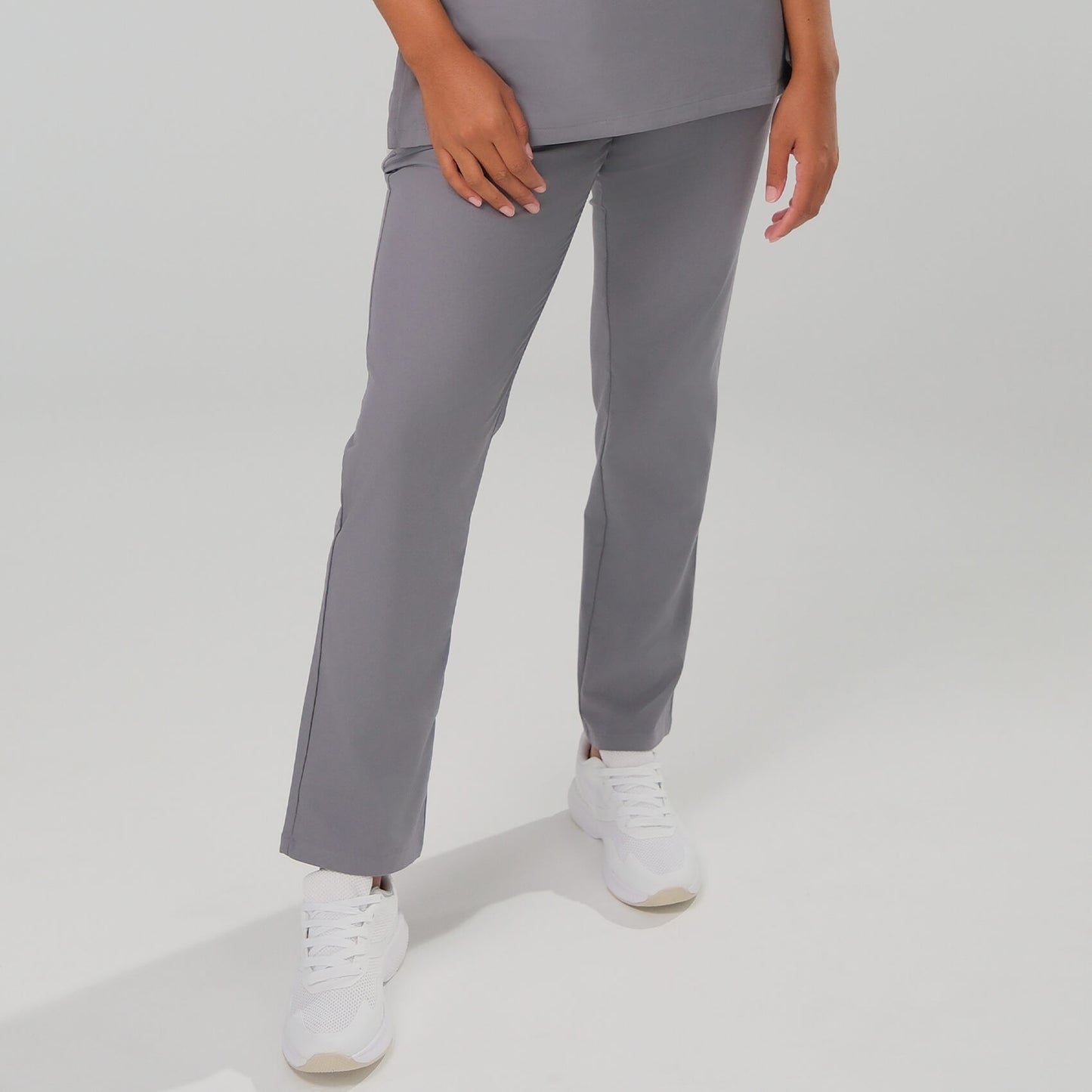 Lady wearing grey scrub trousers with white trainers on a plain background