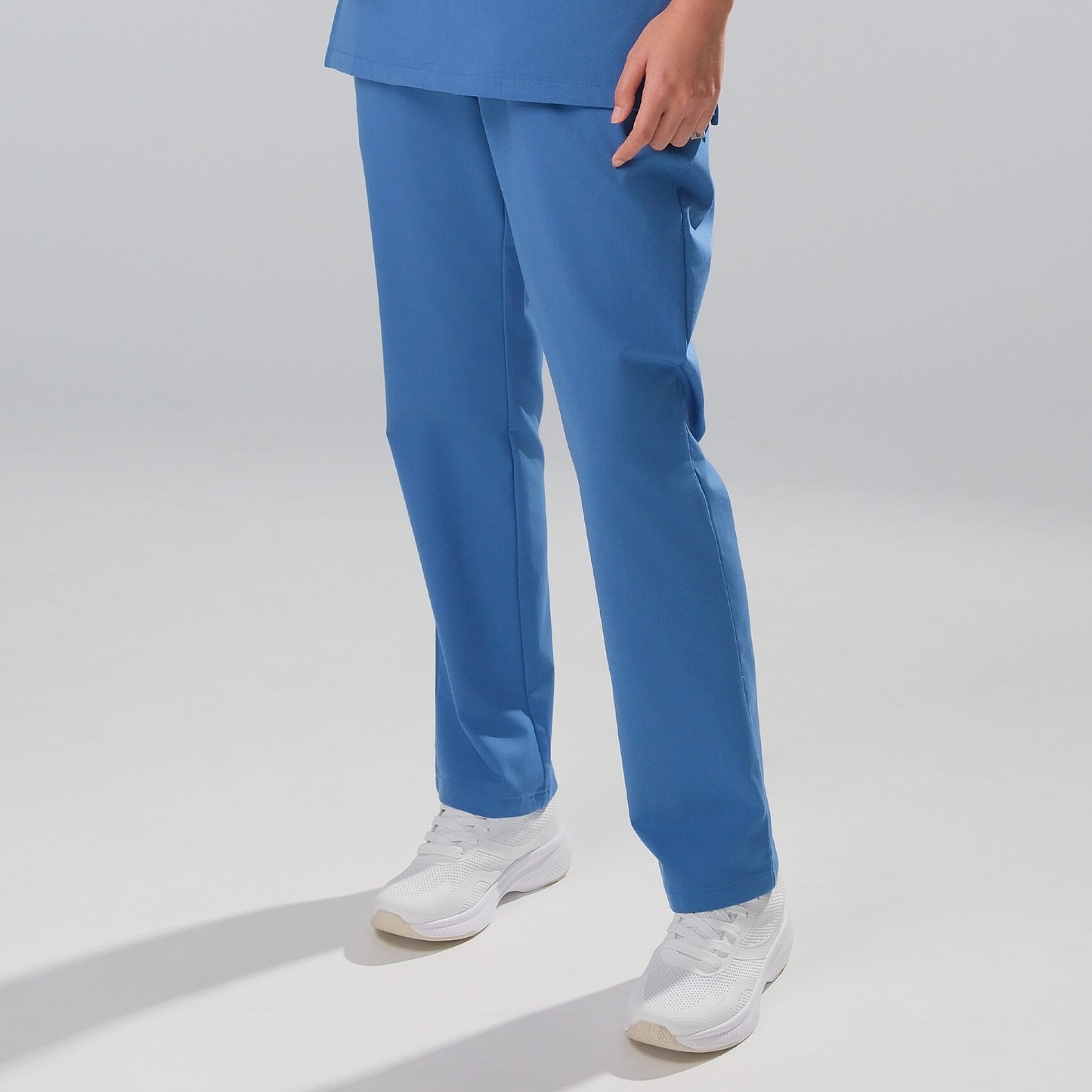 woman wearing blue scrubs and white shoes on a light grey background