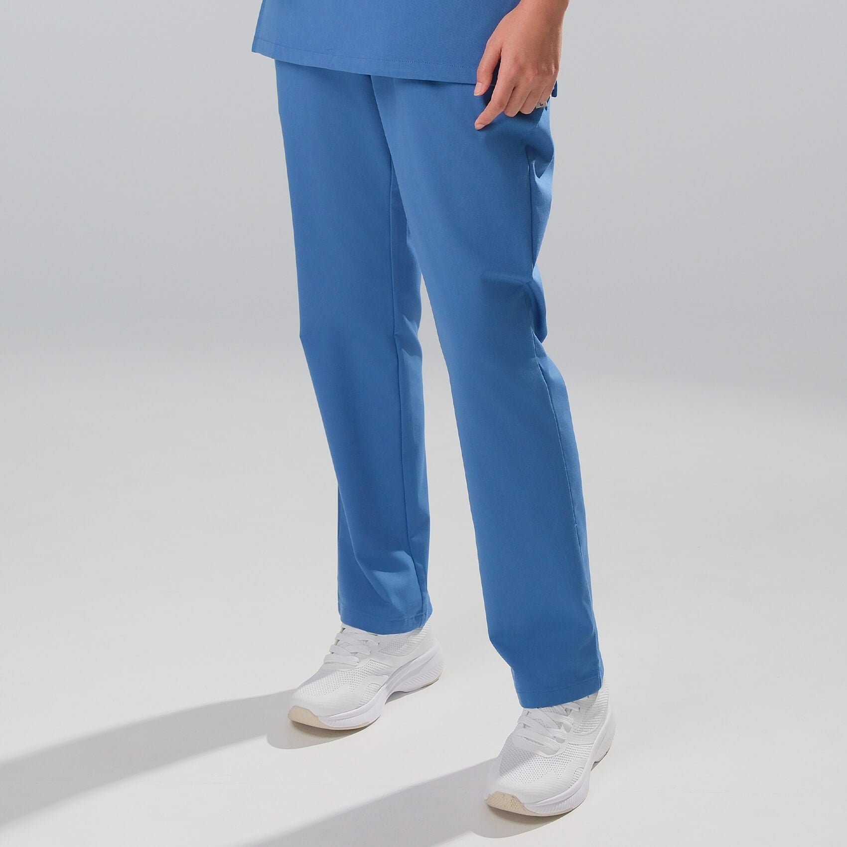woman wearing blue scrubs and white shoes on a light grey background