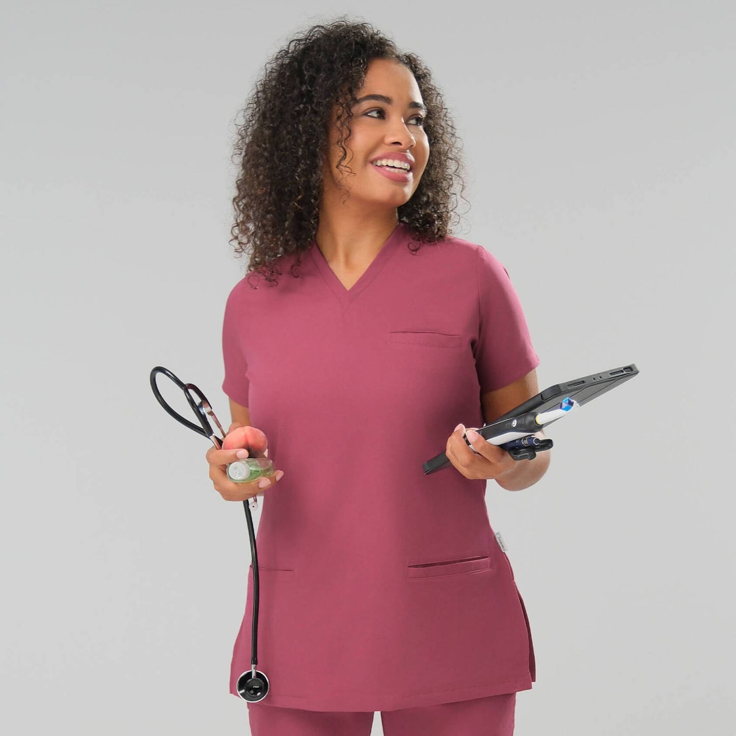 Woman in a red scrub top holding a stethoscope and a tablet .