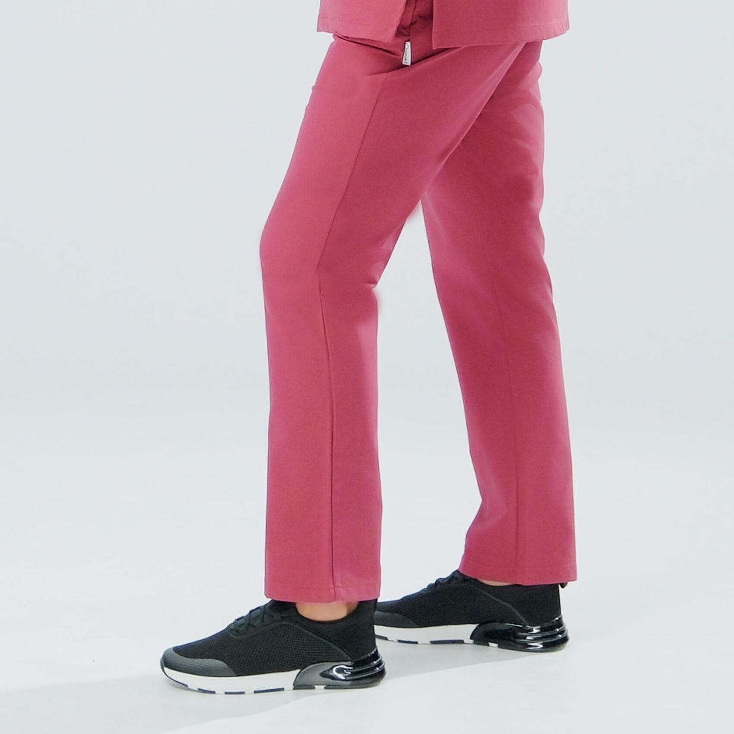 Lady wearing red scrub trousers and black trainers on a white background