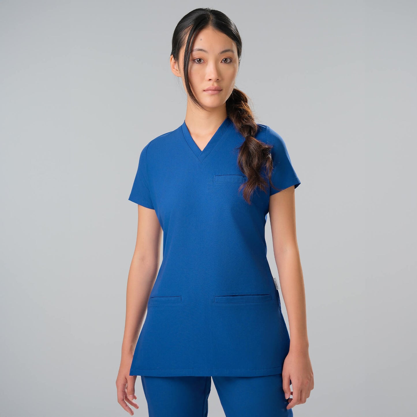 Woman wearing a royal blue scrub set against a grey background